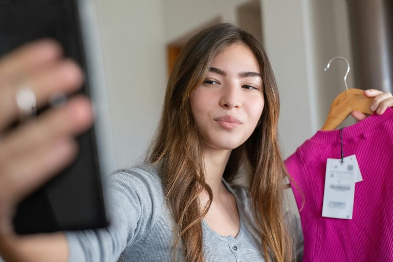 Young woman taking a selfie with a new shirt indoors, showcasing the latest fashion.